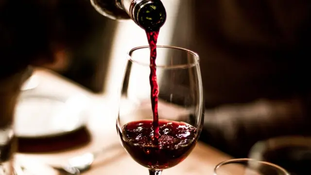 Alguien llenando una copa de vino.