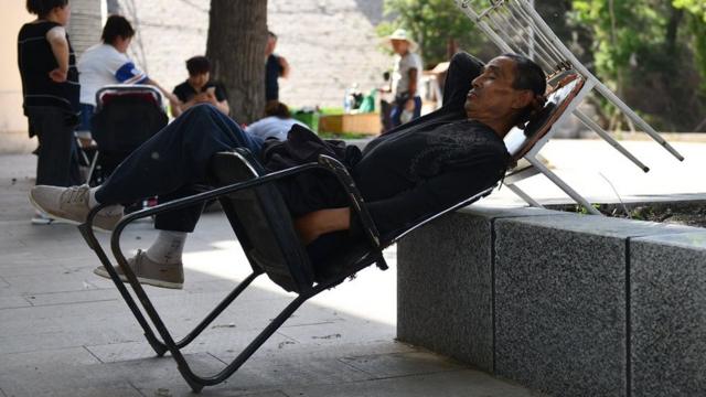 Un Chinois fait la sieste sur une chaise, sur une place publique.