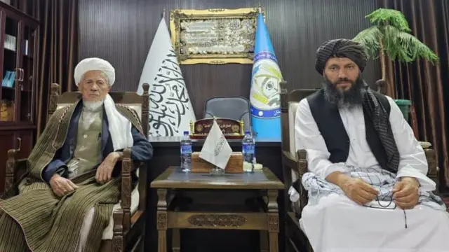 محمد اکبری، معاون شورای علمای شیعه افغانستان در دفتر والی بامیان، در کنار گلحیدر شفق نشسته است.