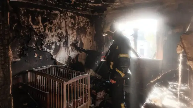 Пожежник стоїть у спаленій кімнаті своєї дитини, дивлячись на ліжко немовляти  