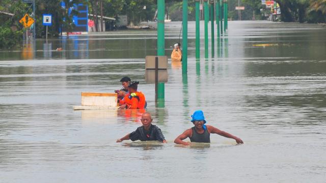 Warga melintasi jalan Pantura yang terendam banjir di Karanganyar, Demak, Jawa Tengah, Minggu (17/3/2024).