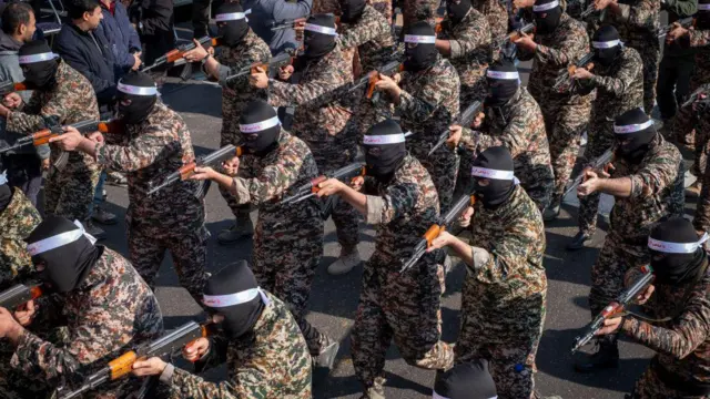 Askeri giysiler ve siyah maskeli Devrim Muhafızları üyeleri bir tatbikat sırasında silahlarını doğrultuyor
