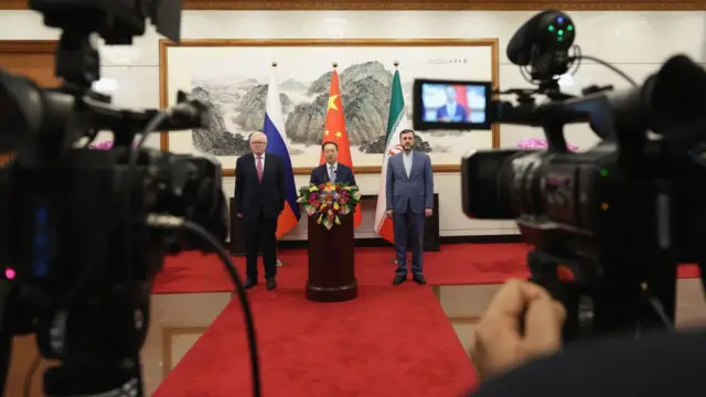 سه مقام ارشد دیپلماتیک روسیه، چین و ایران در یک نشست خبری ایستاده‌اند. از چپ به راست سرگئی ریابکوف، معاون وزیر خارجه روسیه، ما ژائوشو، معاون اجرایی وزیر خارجه چین، و کاظم غریب‌آبادی، معاون وزیر خارجه ایران دیده می‌شوند. آنها پس از دیدار خود در مهمانسرای دولتی دیائویوتای در پکن، در ۱۴ مارس ۲۰۲۵، مقابل میکروفن‌ها و در برابر خبرنگاران سخن می‌گویند. این نشست در چارچوب گفت‌وگوهایی برگزار شد که چین با هدف ازسرگیری مذاکرات متوقف‌شده درباره برنامه هسته‌ای ایران میزبانی کرده بود.