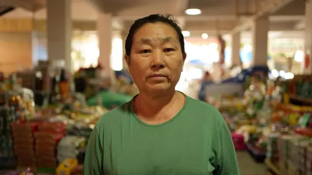 Li Mianzhen,radar betcamiseta verde, no mercado onde ela tem uma barraca.