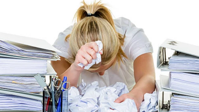 تصویر زنی در میان کاغذها. زن سرش را پایین نگهداشته و کاغذهای مچاله‌ شده را در دست دارد. 