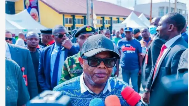 Aworan Alaṣẹ ipinlẹ Rivers, Ajagunfẹyinti Ibok-Ete Ekwe Ibas, ninu ọkan lara ibudo idibo to ṣabẹwo si. O de fila dudu pẹlu igo dudu lojuu rẹ. Aṣọ alawọ aro ni Ajagunfẹyinti Ibas wo, ẹrọ gbohun-gbohun ti awọn oniroyin na siwaju rẹ lasiko to n sọrọ, han ninu aworan yii, bẹẹ ni awọn eeyan wa lẹyin rẹ pẹlu.