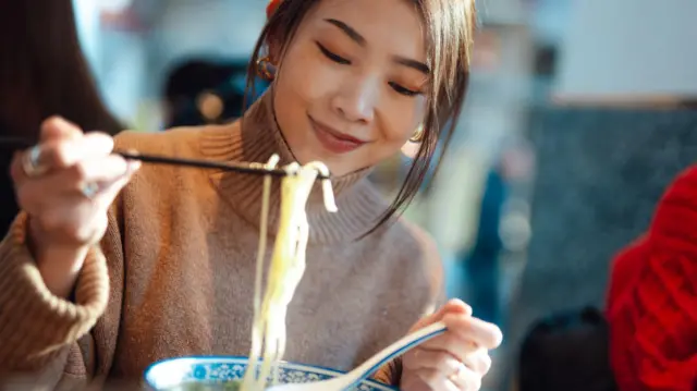 Seorang perempuan menikmati semangkuk mi kuah.