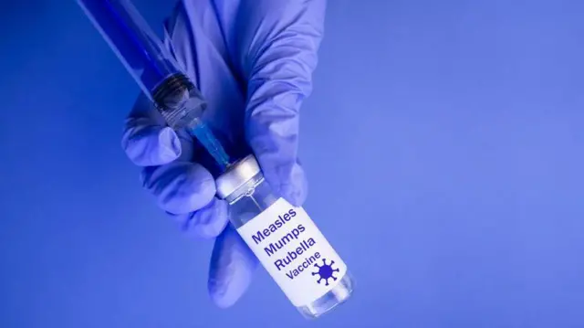 A gloved hand drawing the MMR vaccine out of a bottle