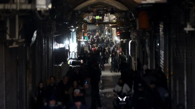 Kolona ljudi koja prolazi pored zatvorenih radnji u mraku