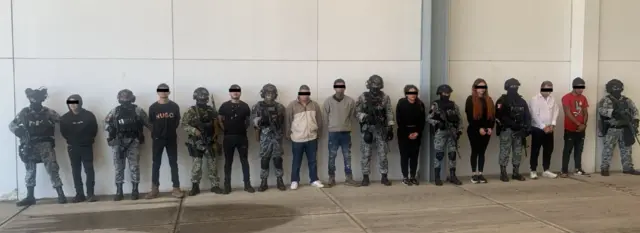 Policías y detenidos posan frente a una pared
