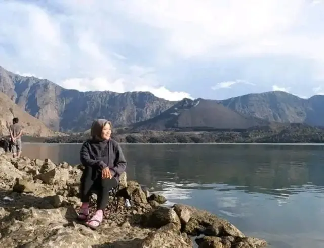 Seorang perempuan berhijab sedang duduk di pinggir danau.