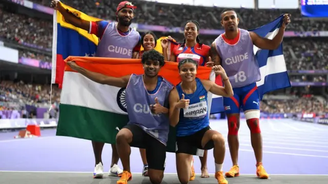 भारत का झंडा हाथ में लिए अभय और सिमरन ज़मीन पर बैठे हैं. उनके पीछे दो महिलाएं और उनके गाइड अपने देशों के झंढों के साथ खड़े हैं.