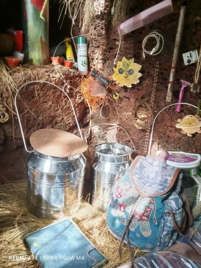 Внутри пещеры, где жила Нина Кутина с детьми: в небольшом углублении между корней дерева стоят несколько металлических сосудов, детский рюкзак и разные предметы, в том числе декоративные