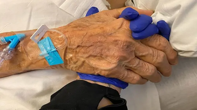 Gabriela holding the hand of a patient during her final hours