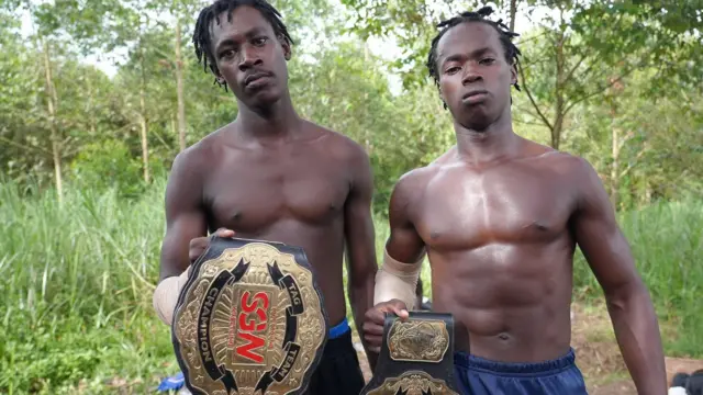 Deux hommes posent torse nu en tenant les ceintures de lutte de la SGW.