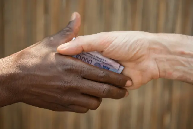 Deux mains qui se saluent avec un billet de 10 000 frs entre elles.
