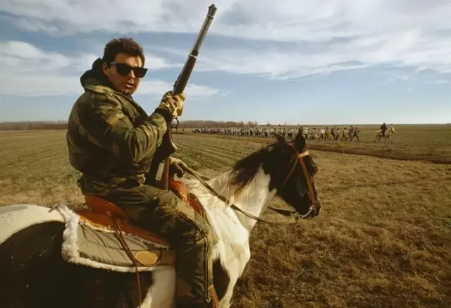 Un homme tenant un fusil assis sur un cheval.