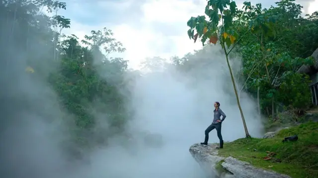 A foto mostra uma mulher na beiracasino legaluma pedra olhando para a floresta rodeadacasino legalneblina.