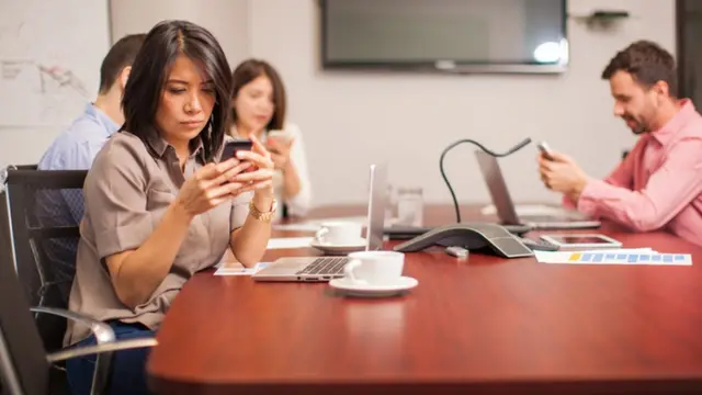 موظفون في غرفة الاجتماعات يستخدمون هواتفهم