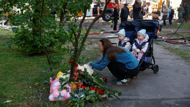 Жінка кладе квіти на меморіал, біля неї коляска з двома дітьми