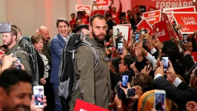 یک تیم امنیتی با لباس شخصی که کوله‌پشتی داشتند، او را احاطه کرده بودند