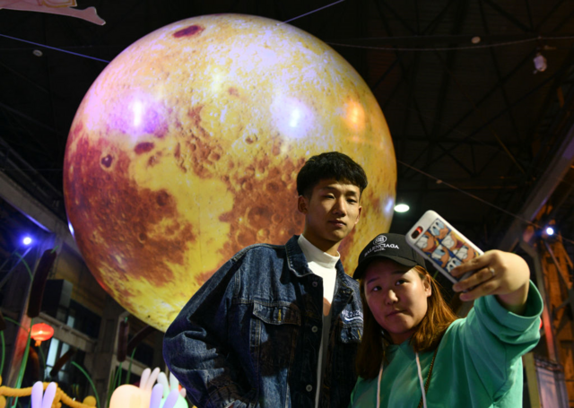 2018年中秋节前夕，中国民众在一个月球状的灯笼前拍照。