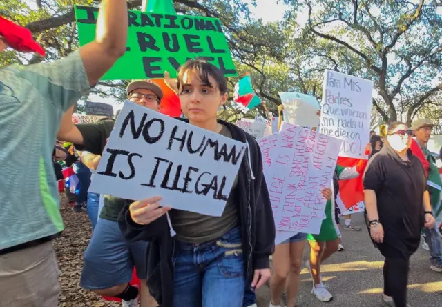 Uma jovem com um cartaz que diz "Nenhum ser humano é ilegal"