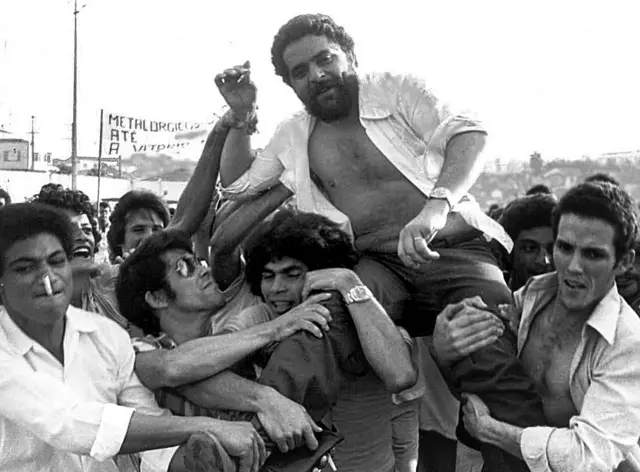 Lula sendo erguido por um grupo de pessoas durante comício.