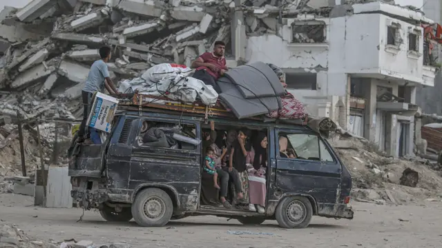 فلسطينيون نازحون يغادرون في حافلة قديمة مدينة غزة مع أمتعتهم، الصورة التقطت نهاراً وسط الدمار.