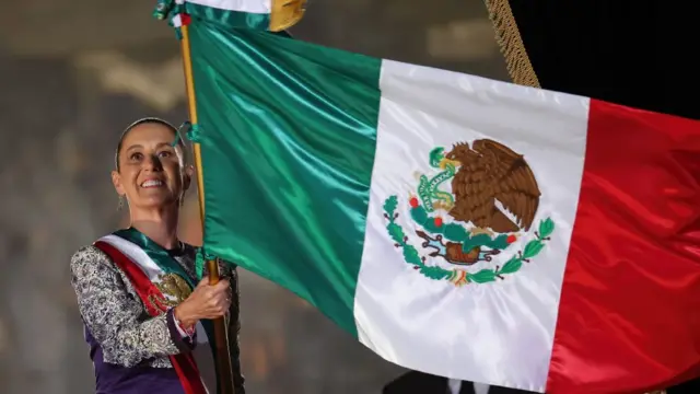 Sheinbaum sonriente sostiene una gran bandera de México