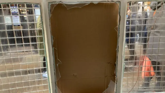 Un primer plano de un cristal de ventana roto, tapado con cartón.