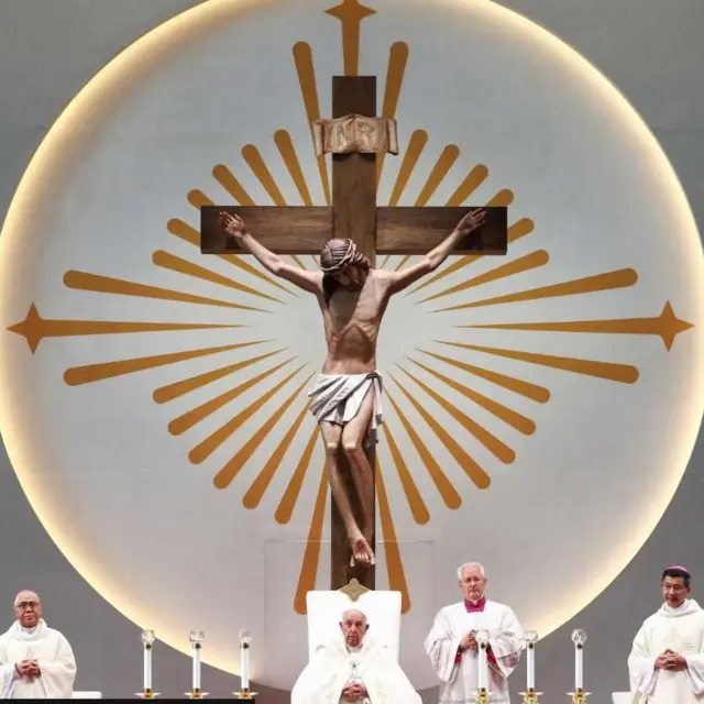 Папа Франциск сидит за столом под Распятием 