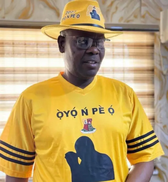 Oriyomi Hamzat wọ asọ T-Shirt alawọ ofeefee ti wọn kọ Oyo n pe ọ siwaju rẹ, o si de fila rẹ bakan naa, o tun lo awo oju