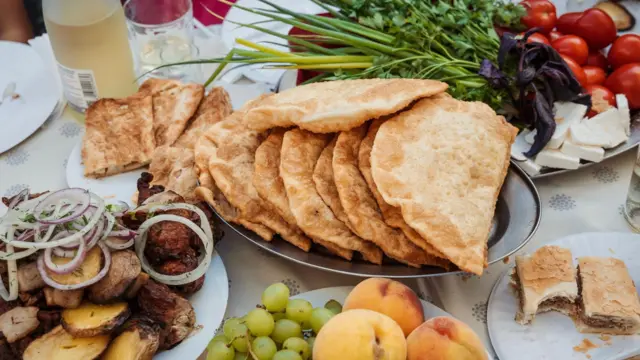 Чебуреки на блюді посередині, поруч овочі, фрукти, напої