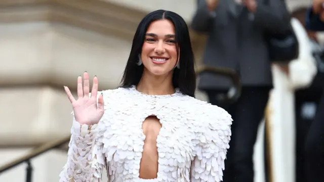 Dua Lipa u beloj haljini sa isečenim delom na dekolteu, puštenom crnom kosom maše publici