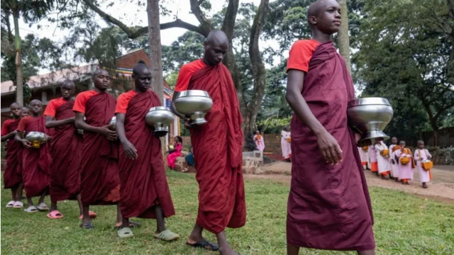Wasu matasan mabiya addinin Buda kenan da suka yi layi za su karɓi hadaya daga al'ummar garin Entebbe a Uganda a lokacin bikukuwan addini na Kathina
