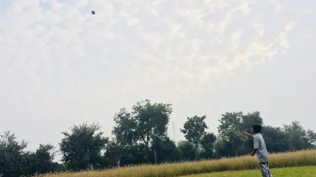 ખેતર વચ્ચે પતંગ ઉડાવતો બાળક