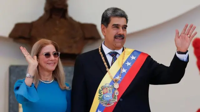 ダークスーツのヴェネズエラ国旗の色や大統領の紋章などをあしらったたすきをかけ、大統領職を表す飾りをつけたマドゥロ氏が笑顔で左手を挙げ、隣で青いドレス姿のシリア夫人も笑顔で手を挙げている
