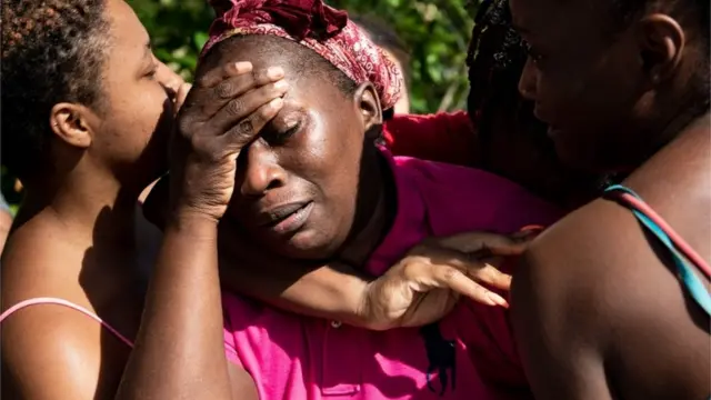 A woman in the Bahamas holds her head in her hands as she is greeted by loved ones following Hurricane Dorian