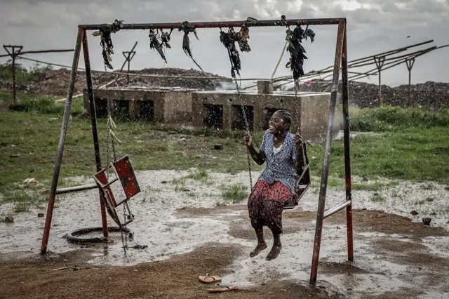 Mulher sentada em um balanço em ambiente aberto, em dia de chuva