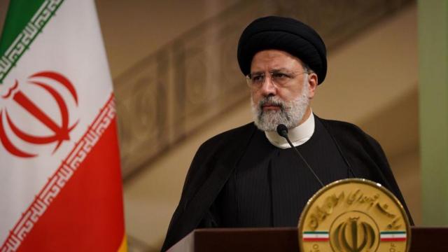 Ebrahim Raisi, presidente do Irã, que faleceu em um acidente de helicóptero no último domingo (19/5). Na imagem, ele está em frente a um microfone e com a bandeira do país ao fundo