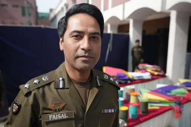 Faisal Kamran in his police uniform stands in front of a brightly coloured table which is lined with confiscated kites and rolls of string