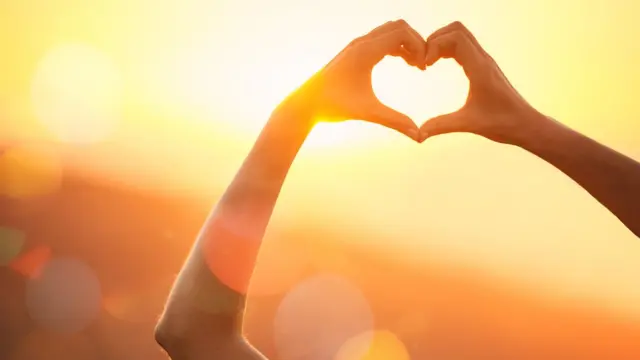 Una mujer alzando los brazos haciendo el gesto del corazón.