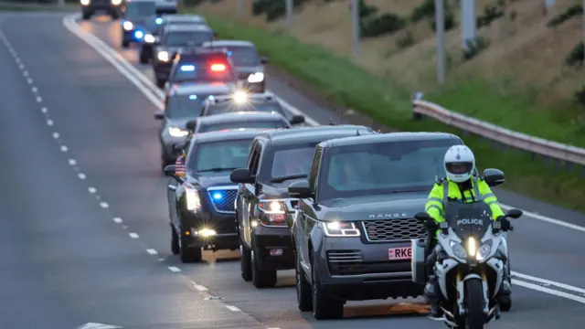 Колона чорних автомобілів їде дорогою, а попереду - поліцейський мотоцикліст