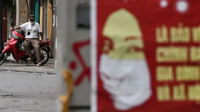 A government poster warning about Covid-19 and a man sitting on a motorcycle