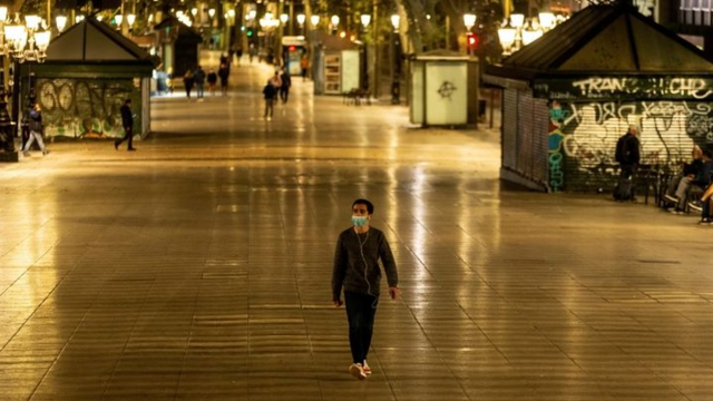 Homem de máscara caminha em rua de pedestres à noite