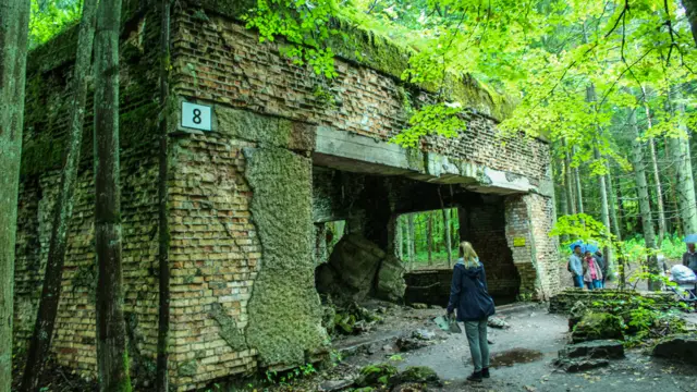 Turista observa monumento coberto por floresta no Wolfsschanze