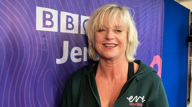 La imagen muestra a Trudi Roscouet vistiendo una sudadera con capucha negra, con la marca 'eve studios', sonriendo con cabello rubio corto, junto a un fondo morado de BBC Jersey.