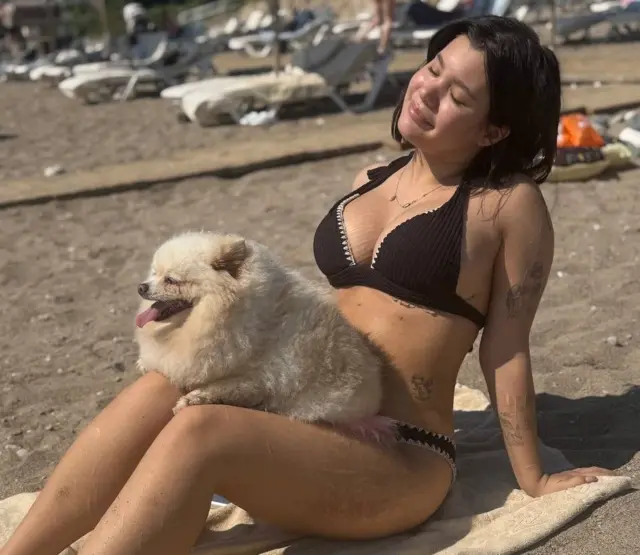 Девушка в купальнике на пляже, на коленях у нее собака