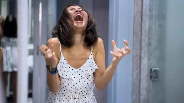 সাদা জামা পরা এক নারী হাত মুষ্টিবদ্ধ করার ভঙ্গিতে ও চিৎকার করে তীব্র রাগ প্রকাশ করছে 